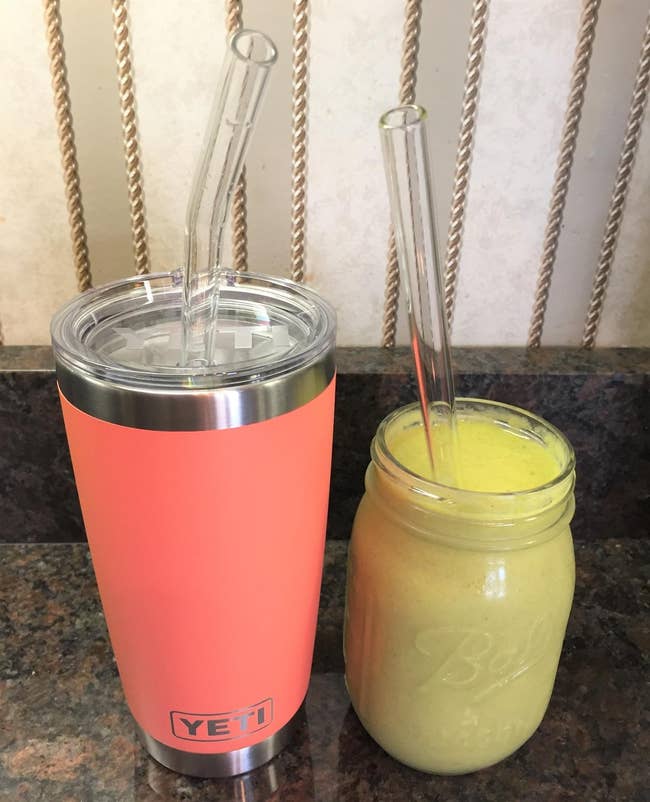 a reviewer photo of a Yeti tumbler with a glass bent straw inserted, and a mason jar with a straight glass straw inserted 