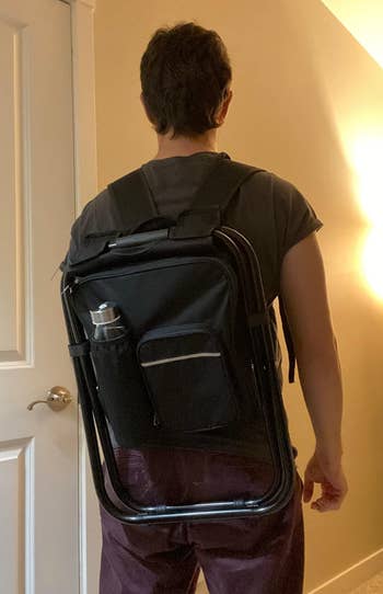 Person with a black backpack featuring multiple compartments and a side water bottle pocket