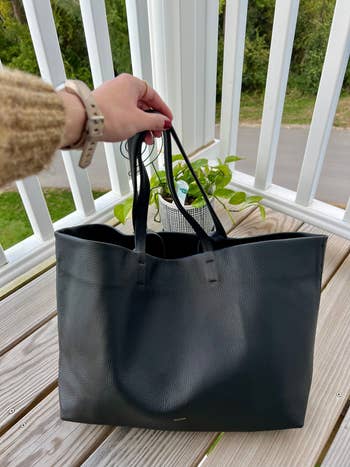 me, showing the front side of the black tote bag with long and short handles