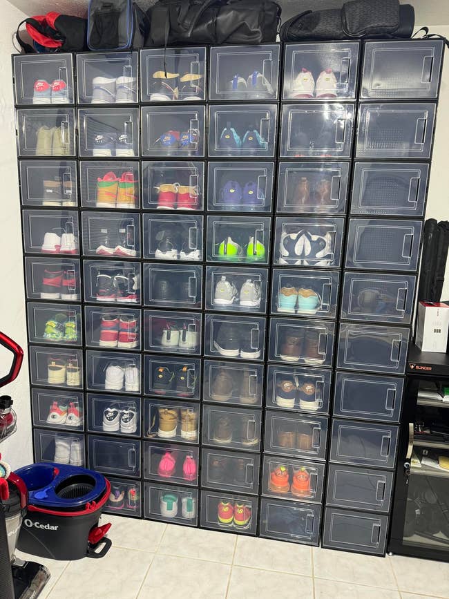 Wall of transparent shoe storage boxes with various sneakers, organized and displayed in a home