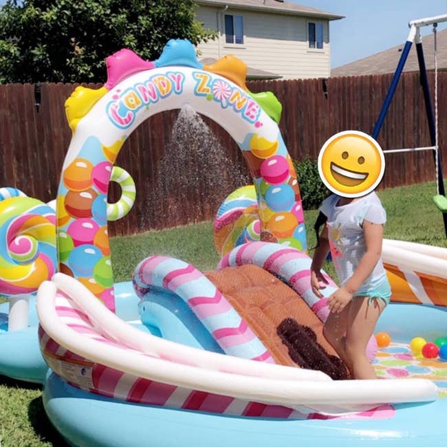 Child plays astatine  inflatable candy-themed h2o  playset successful  backyard. The setup includes slides and candy decorations. House and plaything  acceptable   successful  background