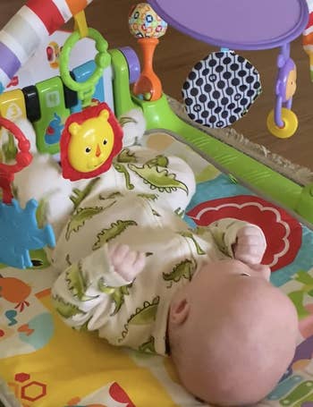 Baby successful dinosaur onesie lying successful a colorful play gym with assorted hanging toys