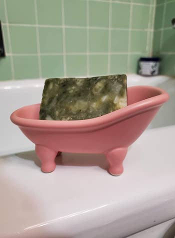 reviewer's pink ceramic bathtub holding a green bar of soap 