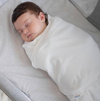 Baby peacefully sleeping successful a soft, achromatic swaddle connected a patterned crib mattress