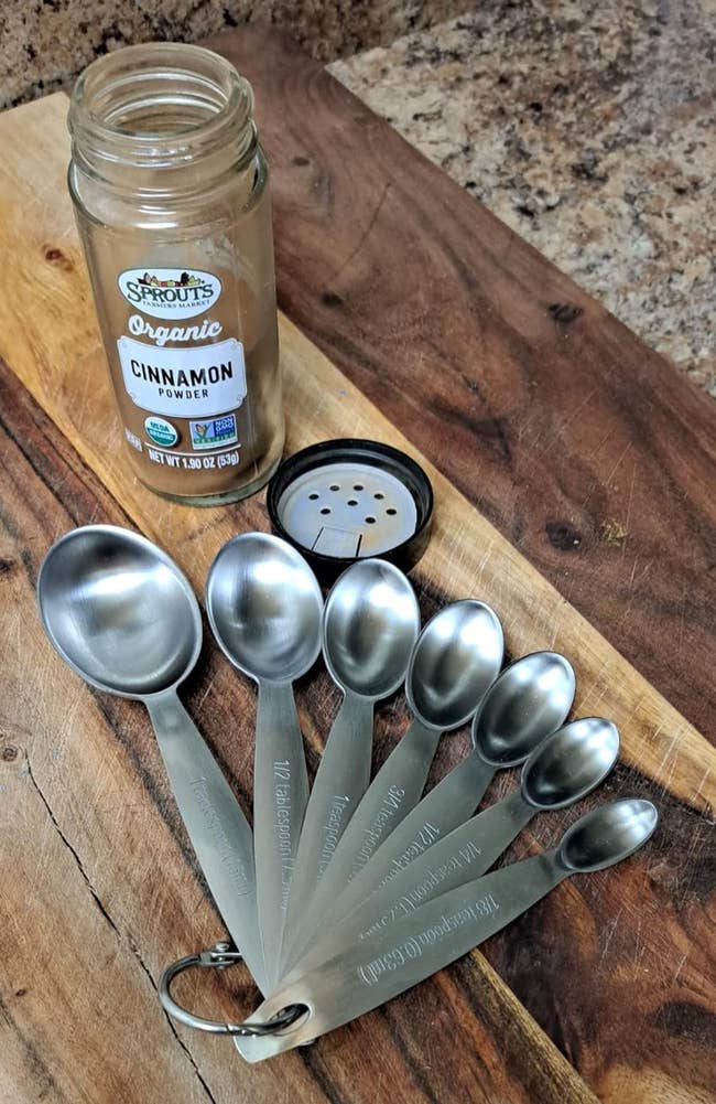 reviewers seven stainless steel measuring spoons next to a glass jar of cinnamon