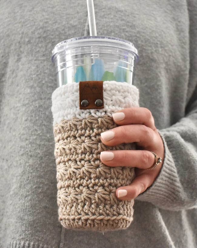 model holding a cold cup with a knit oatmeal colored sleeve around it 