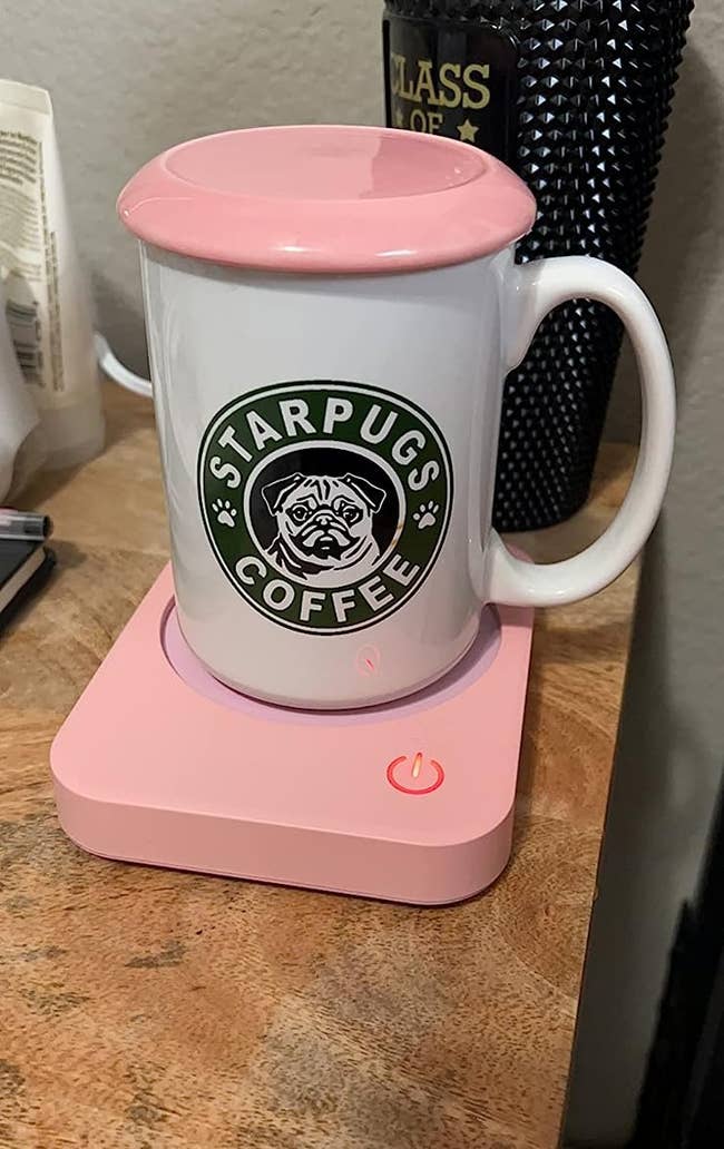 The reviewer's white coffee mug on top of pink mug warmer