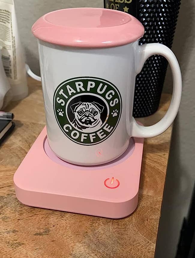 The reviewer's white coffee mug on top of pink mug warmer