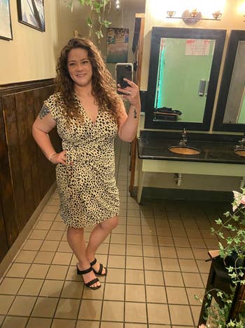 Person in a patterned dress and sandals taking a selfie in a restroom mirror