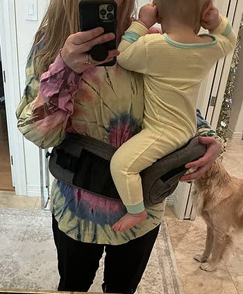 reviewer showing how the carrier wraps around their waist and make it easy to hold a baby