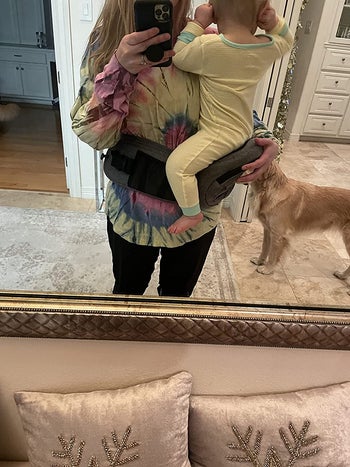 reviewer showing how the carrier wraps around their waist and make it easy to hold a baby