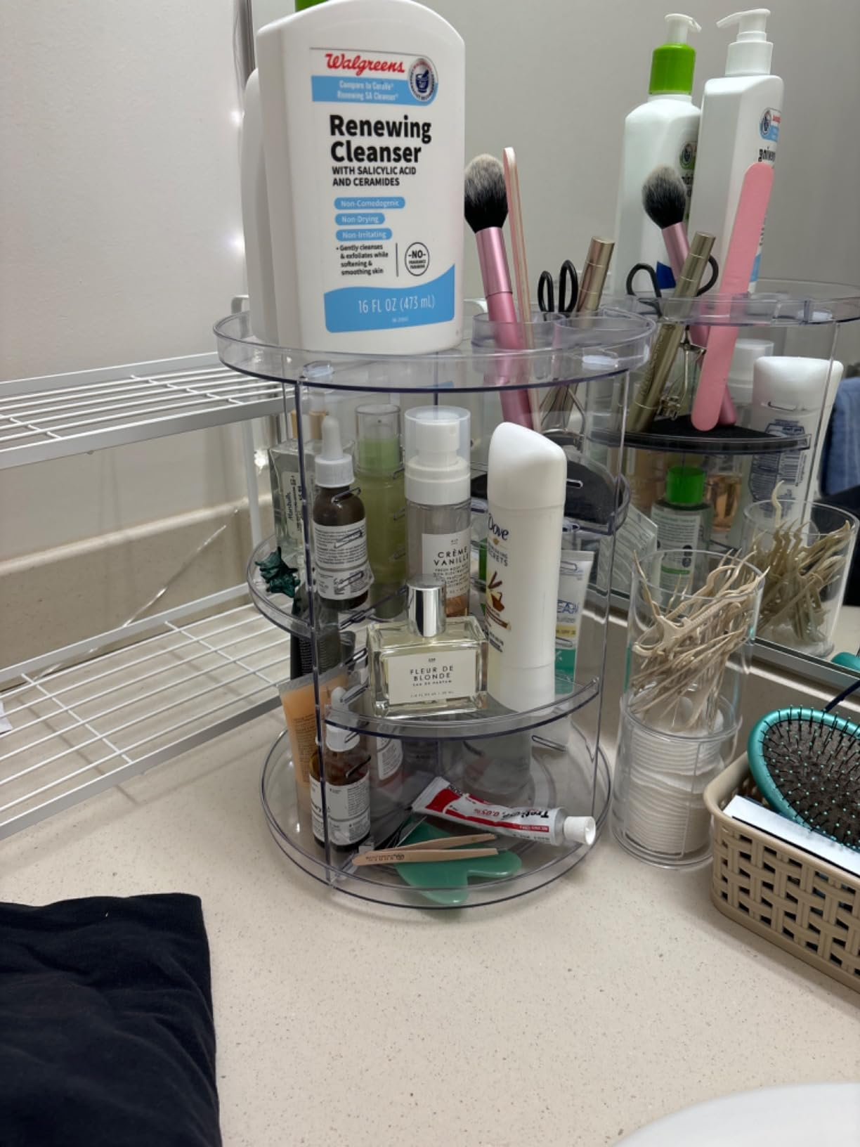 Rotating organizer connected  a bath  antagonistic  holding skincare products, brushes, and toiletries. Nearby are a comb and a handbasket  with fabric  swabs