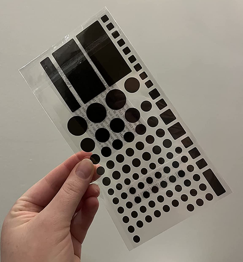reviewer holding the sheet of dimming covers, which come in assorted shapes and sizes
