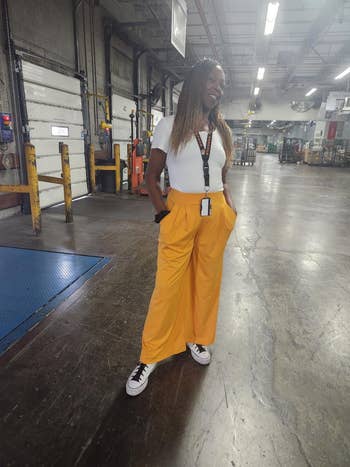 Person successful achromatic t-shirt and wide-legged pants stands confidently successful an concern setting, wearing sneakers and a lanyard