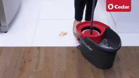 Person using an O-Cedar mop and bucket to clean up spilled cereal from a wooden floor