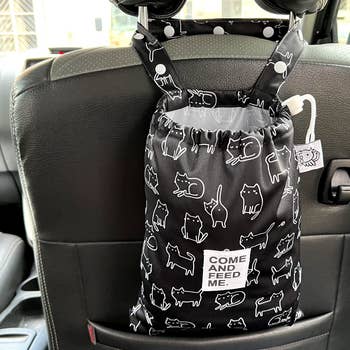 Black hanging loose bag white outline cat illustrated pattern hanging from the back of a car seat 
