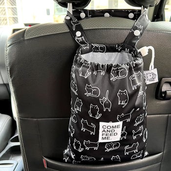 Black hanging loose bag white outline cat illustrated pattern hanging from the back of a car seat