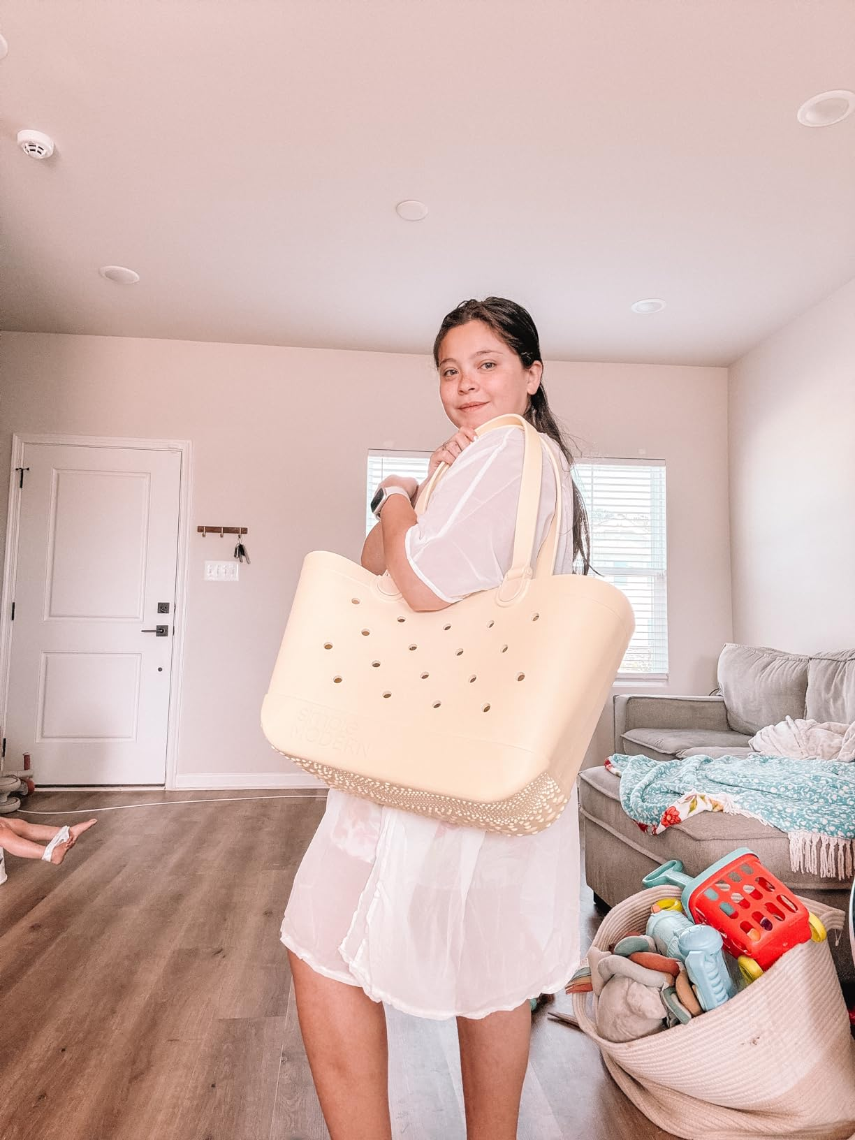 Person lasting  successful  a surviving  room, holding a ample  tote bag. Dressed casually successful  sheer clothing, with children's toys disposable   successful  the background