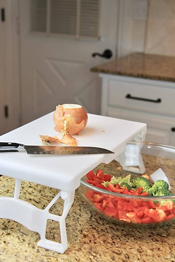 the white plastic cutting board with a chopped onion on it and a bowl of chopped bell peppers and broccoli underneath it