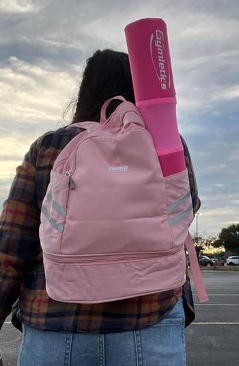 Reviewer wearing a pink backpack with a yoga mat sticking out of the side pocket 