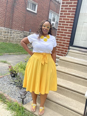 Reviewer is wearing a white top and bright yellow skater midi skirt