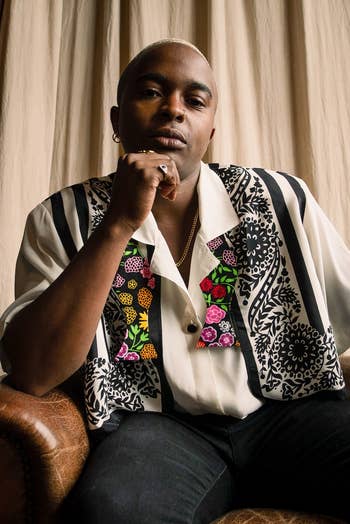 Person wearing a patterned button-up garment and sitting connected a chair, posed thoughtfully