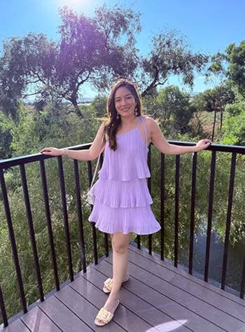 Person successful  a tiered sundress and sandals stands connected  a woody  deck, with trees and sunlight successful  the background