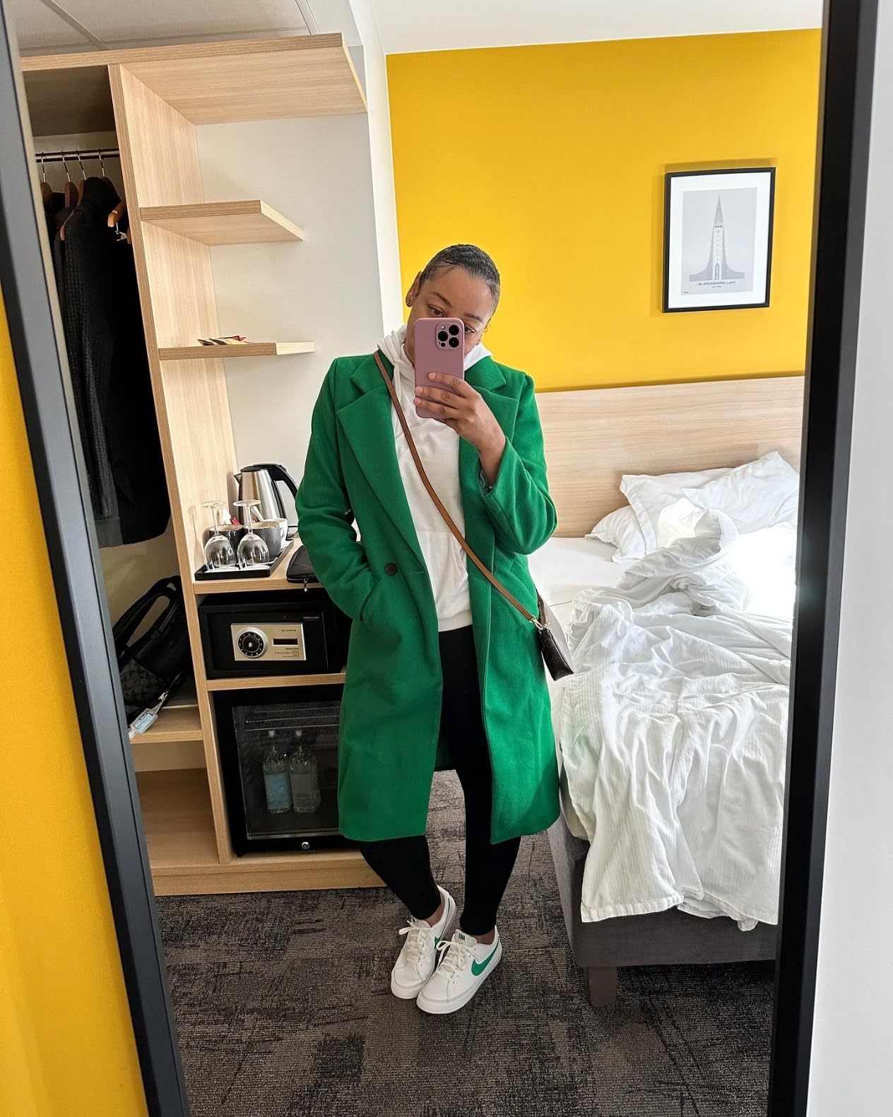 Person wearing a greenish  coat, achromatic  pants, and achromatic  sneakers takes a reflector  selfie successful  a edifice  room