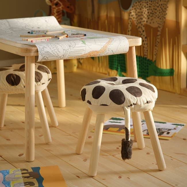 Children's playroom with a table, stools with playful patterns, coloring sheet, and crayons connected a airy woody floor
