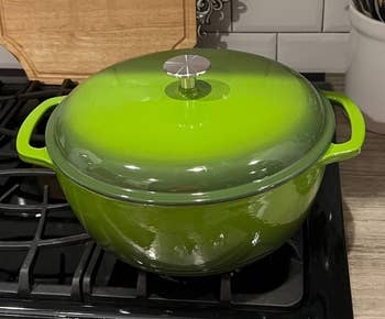 Green cast iron Dutch oven on stovetop, with shiny lid and side handles. Ideal for cooking and baking. Featured in a shopping article