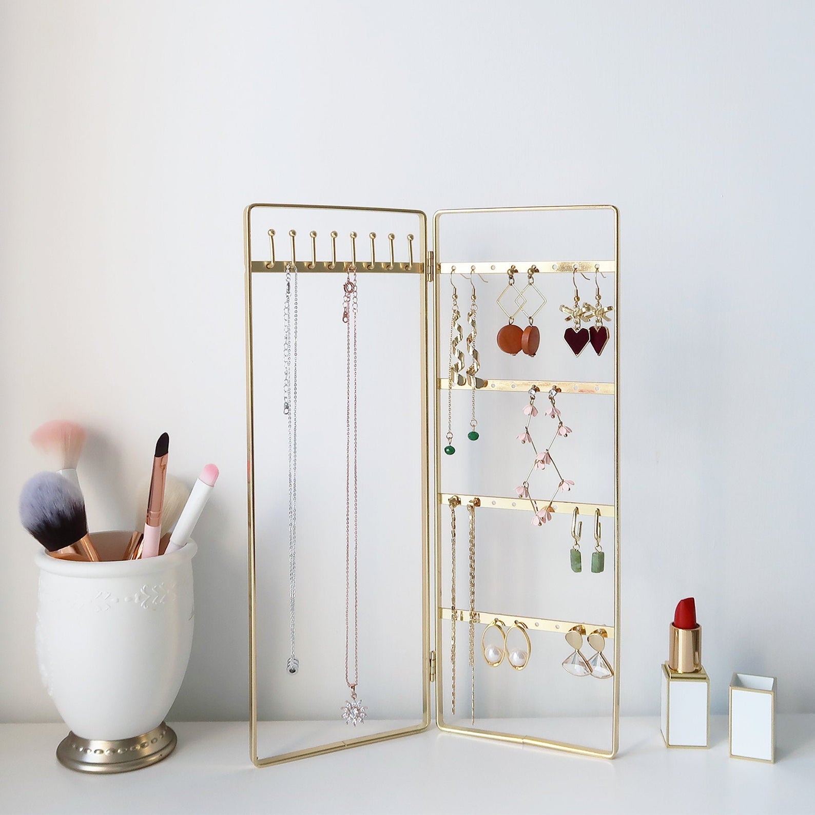 The gold bi-folding jewelry stand on a counter with baubles hanging off it