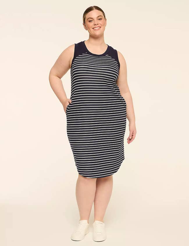 Woman successful a casual striped sleeveless formal with pockets and achromatic sneakers, lasting and smiling against a plain background
