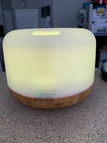 Essential oil diffuser with illuminated top and wood finish base on bathroom counter