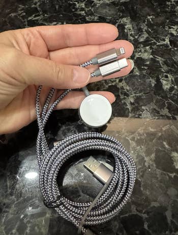 Hand holding a braided multi-device charging cablegram  with USB end, featuring connectors for Lightning, USB-C, and Magnetic charging