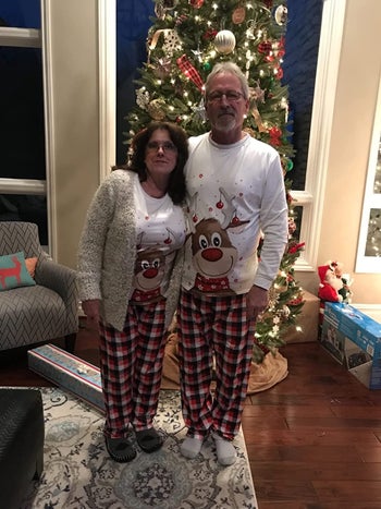a man and woman standing in front of a christmas tree in matching pajamas