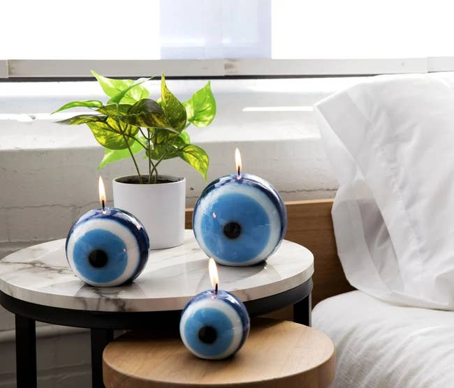Thee lit evil eye candles of different sizes resting on a nightstand