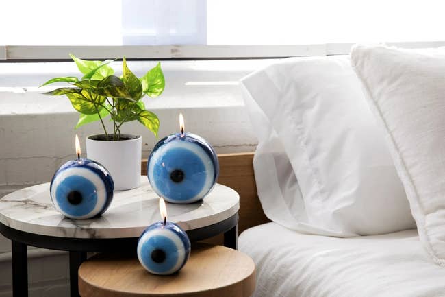 Thee lit evil eye candles of different sizes resting on a nightstand