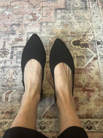 Person wearing stylish achromatic flats with a ribbed texture connected a patterned rug