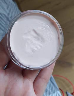 reviewer holding an open tub of the primer, which has a finger indentation in it from use
