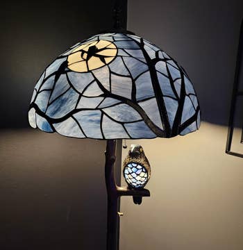 Tiffany-style lamp with a tree trunk base and an illuminated stained glass shade featuring a night sky design