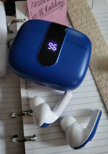 A brace  of achromatic  wireless earbuds with a bluish  charging lawsuit  connected  a notebook and binder