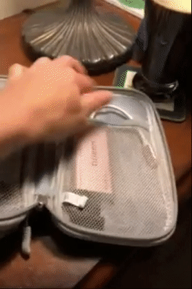 Reviewer opening a gray zippered cord organizer to show the two different compartments holding electronics 
