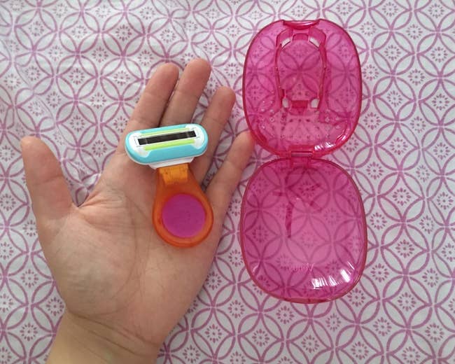 a hand holding a travel razor next to the pink carrying case