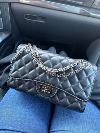 Quilted handbag with chain strap on a person's lap inside a vehicle
