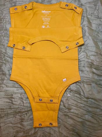 Yellow babe  bodysuit with drawback   buttons displayed connected  a cloth  background
