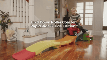 GIF of child model riding red scooter down a multi-colored ramp