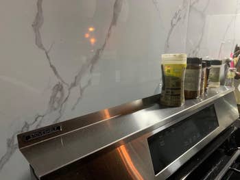 Spice jars neatly arranged connected  a support  supra  a stovetop against a marble-patterned backsplash