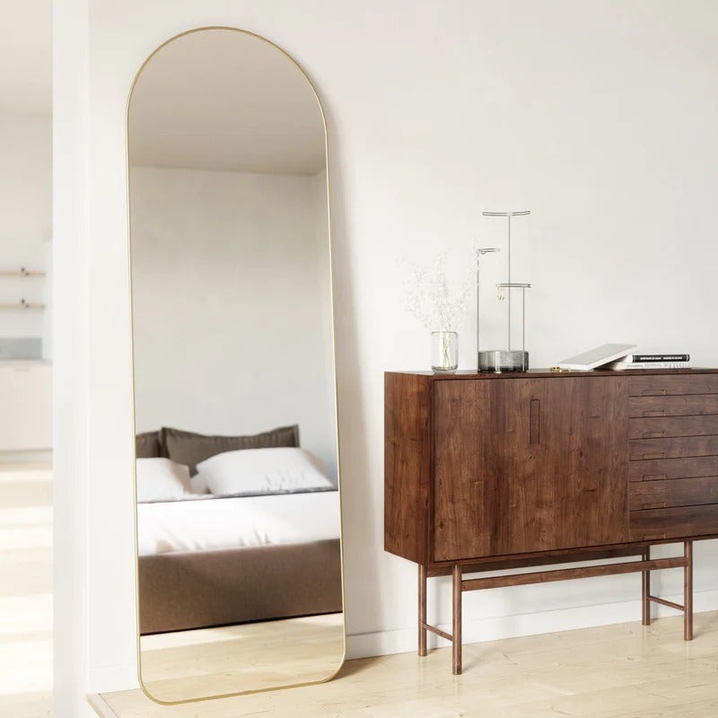 the standing mirror, which has a curved top and rounded brass rim