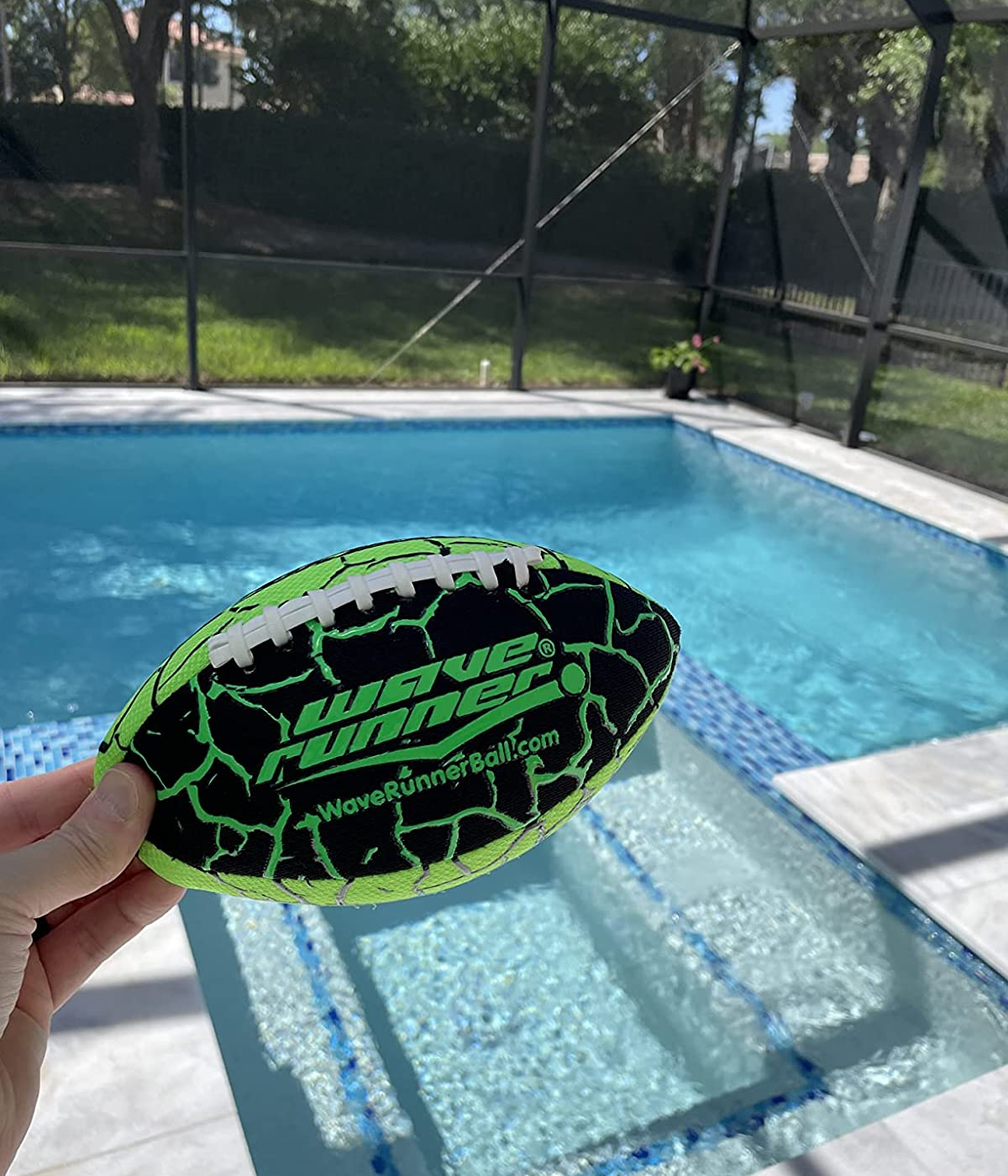 reviewer photo of them holding a green and black wave runner football up in front of their in-ground pool