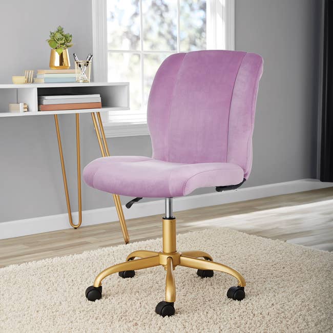 Modern swivel office chair with plush upholstery and gold base on beige rug. Shelves with decor visible in the background